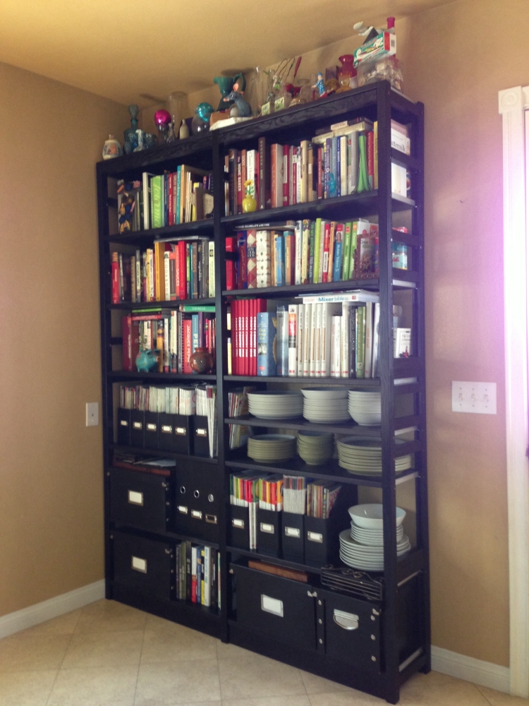 Black tall solid wood bookcase used for cookbooks and dishware in a kitchen
